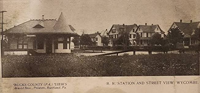 An early printed postcard captioned “R. R. Station and Street View, Wycombe” — the railroad station at left and a row of gabled houses along the street beyond the track.
