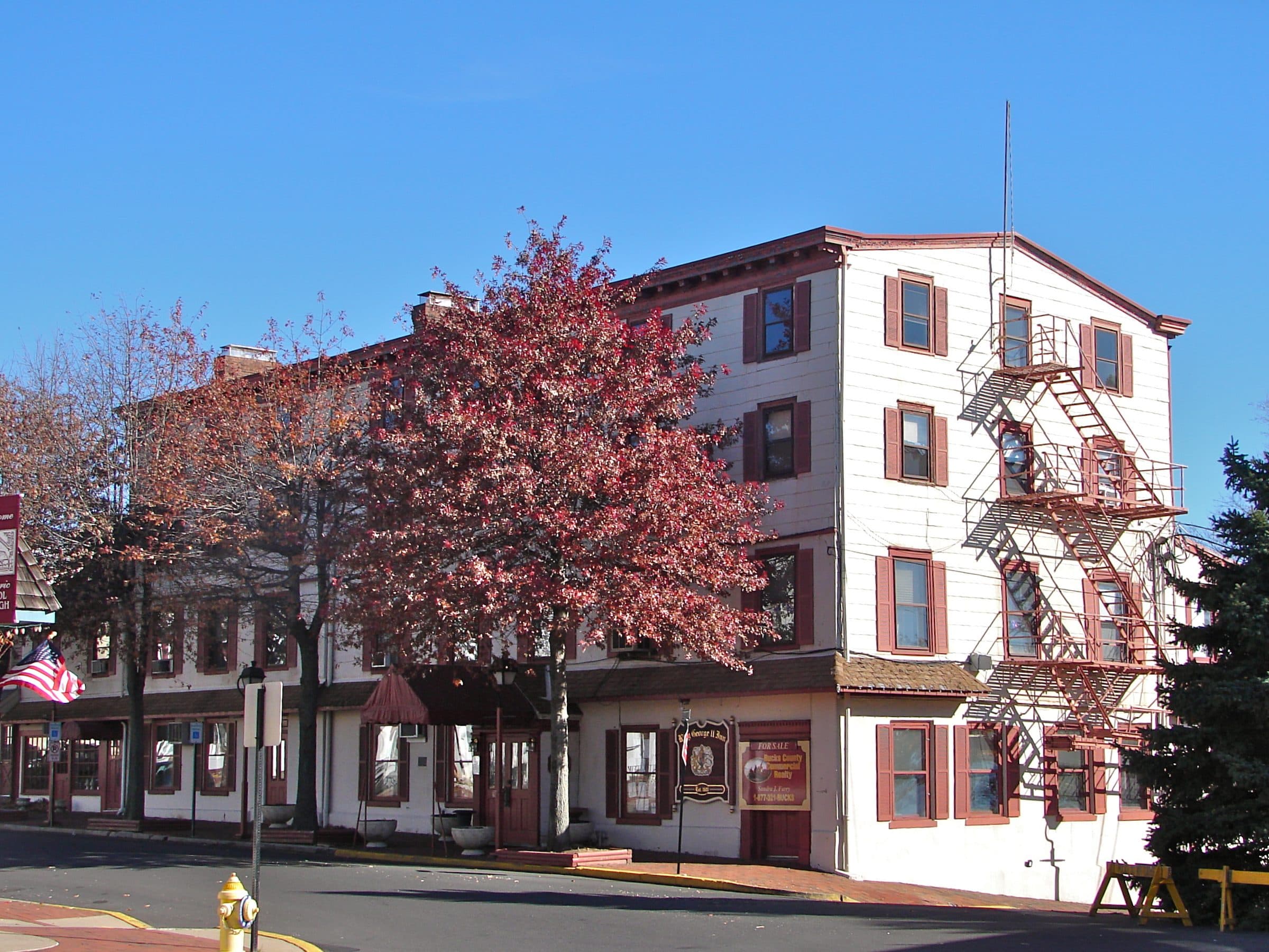 The King George II Inn on Radcliffe Street in Bristol, Pennsylvania — a three-story white clapboard building with red shutters and an iron fire escape, on the corner in autumn.