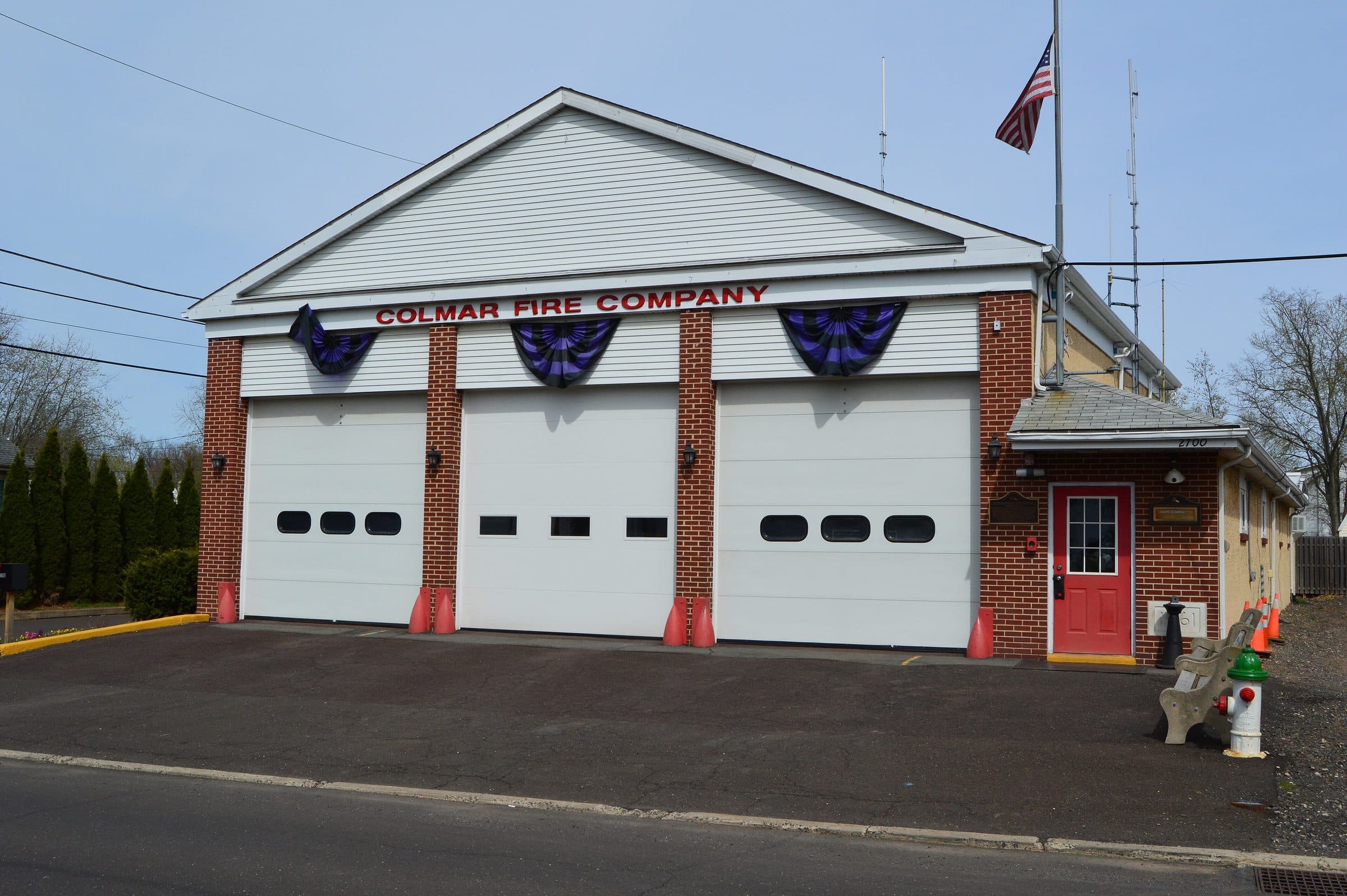 The Colmar fire company station in Pennsylvania — a brick engine house with three white bay doors hung with red, white and blue bunting.