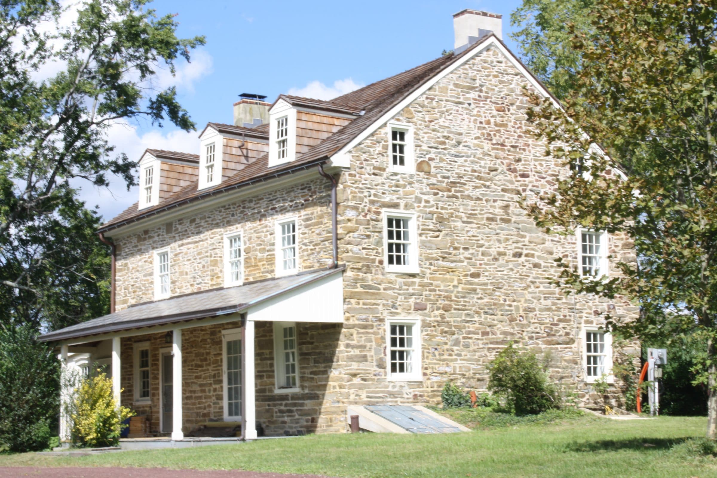 Knapp Farm in Montgomeryville, Pennsylvania — a two-and-a-half-story fieldstone farmhouse with dormer windows and a shingled porch, standing on open lawn.
