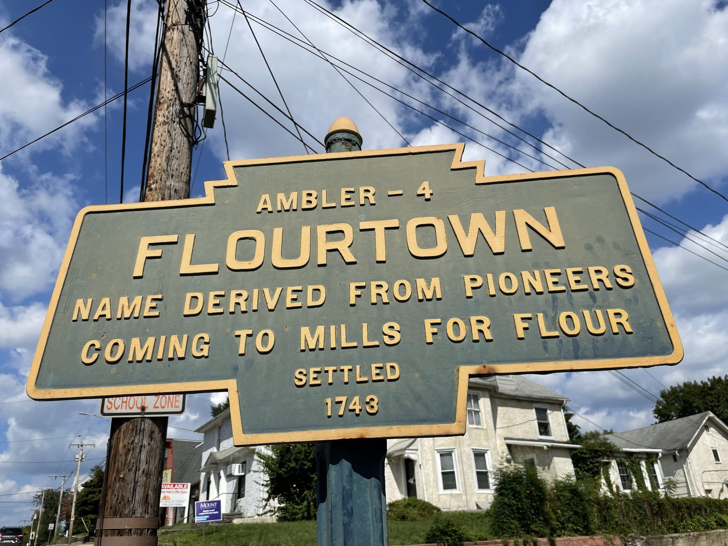 The Pennsylvania keystone marker on Bethlehem Pike reading “Flourtown — name derived from pioneers coming to mills for flour, settled 1743”, with white frame houses behind it.