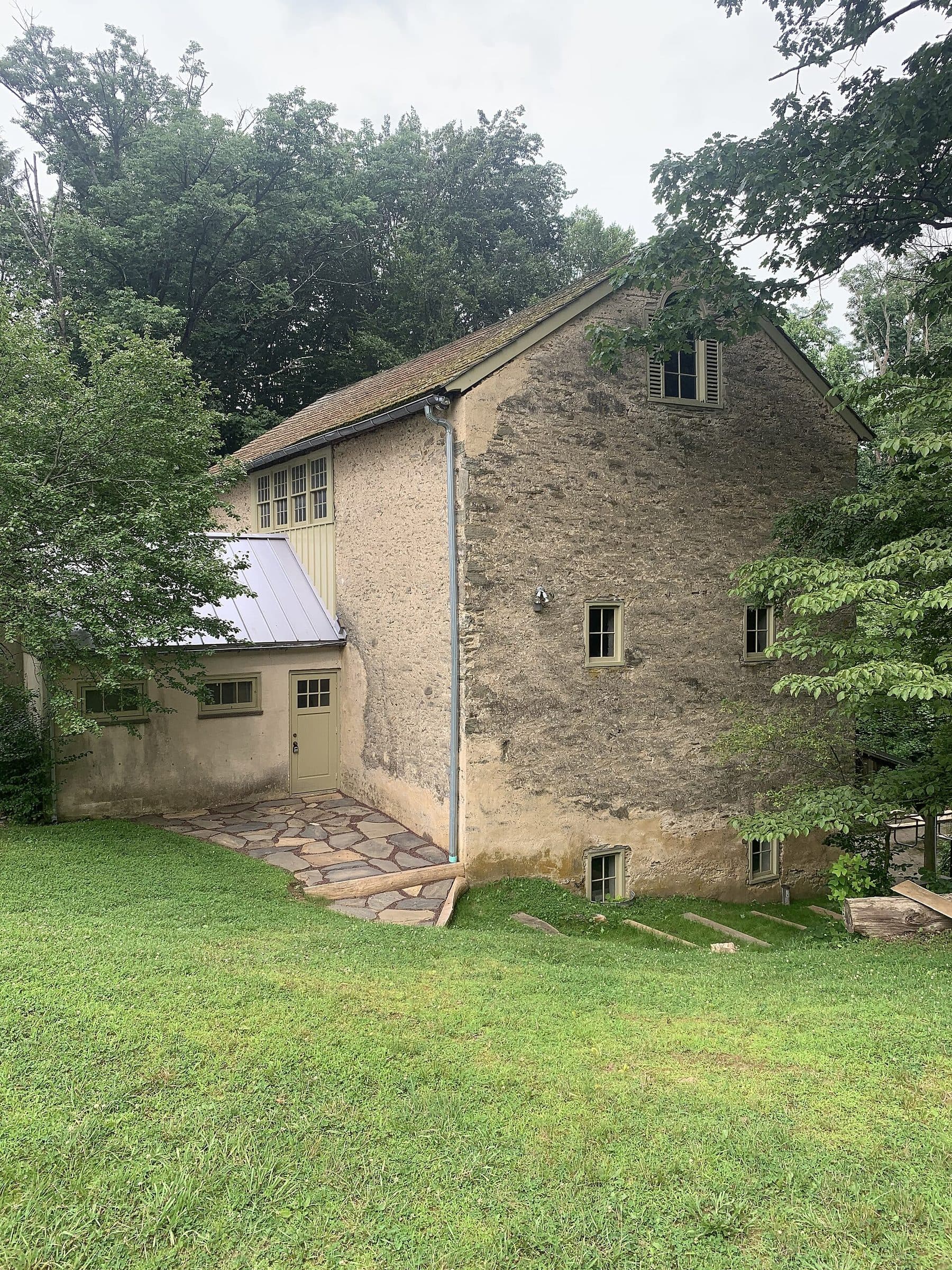 The stone carriage house at Saunders Woods in Gladwyne, Pennsylvania, its rendered gable end and small windows facing an open lawn among trees.
