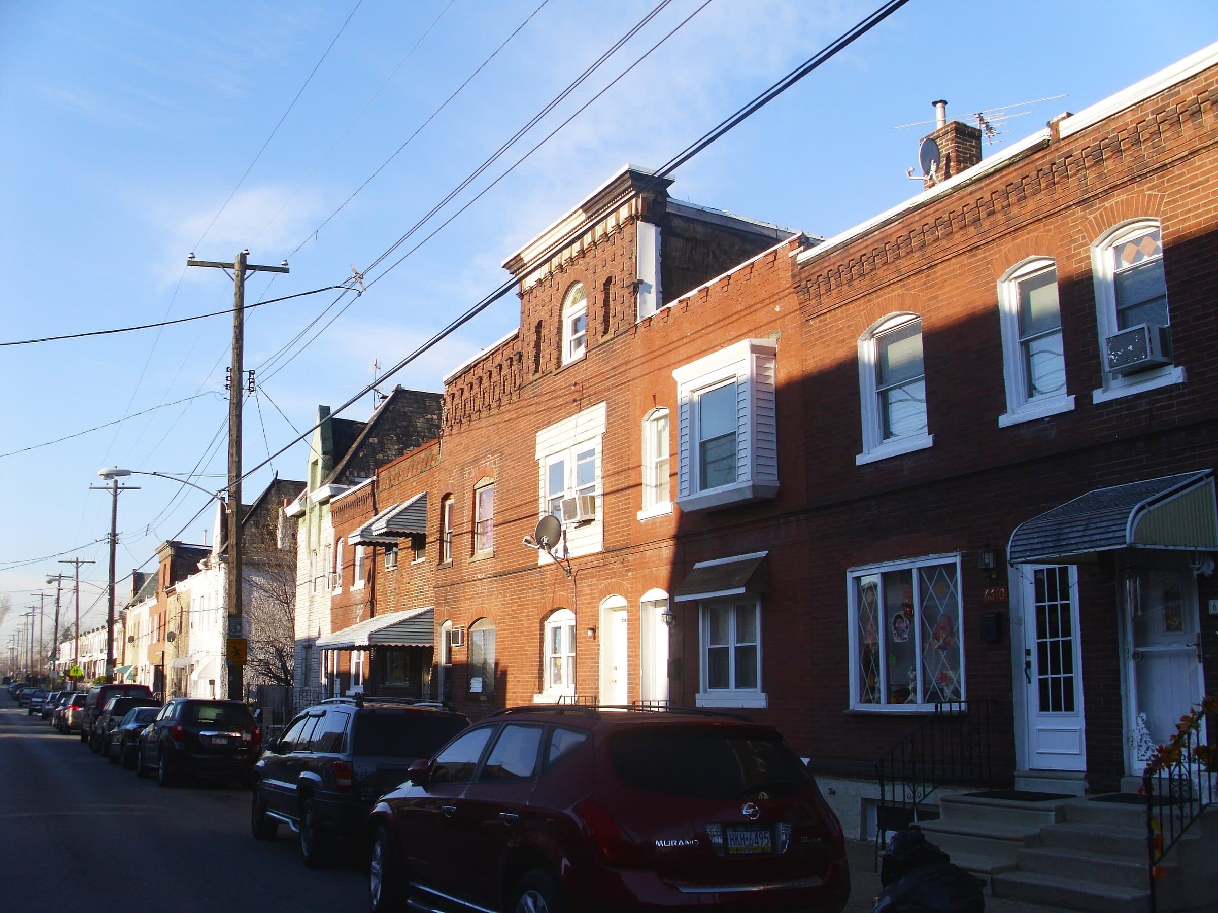 Castle Row on the 6600 block of Tulip Street in Tacony, Philadelphia — a terrace of 1880s brick houses with bay windows and cornices, cars parked along the curb.