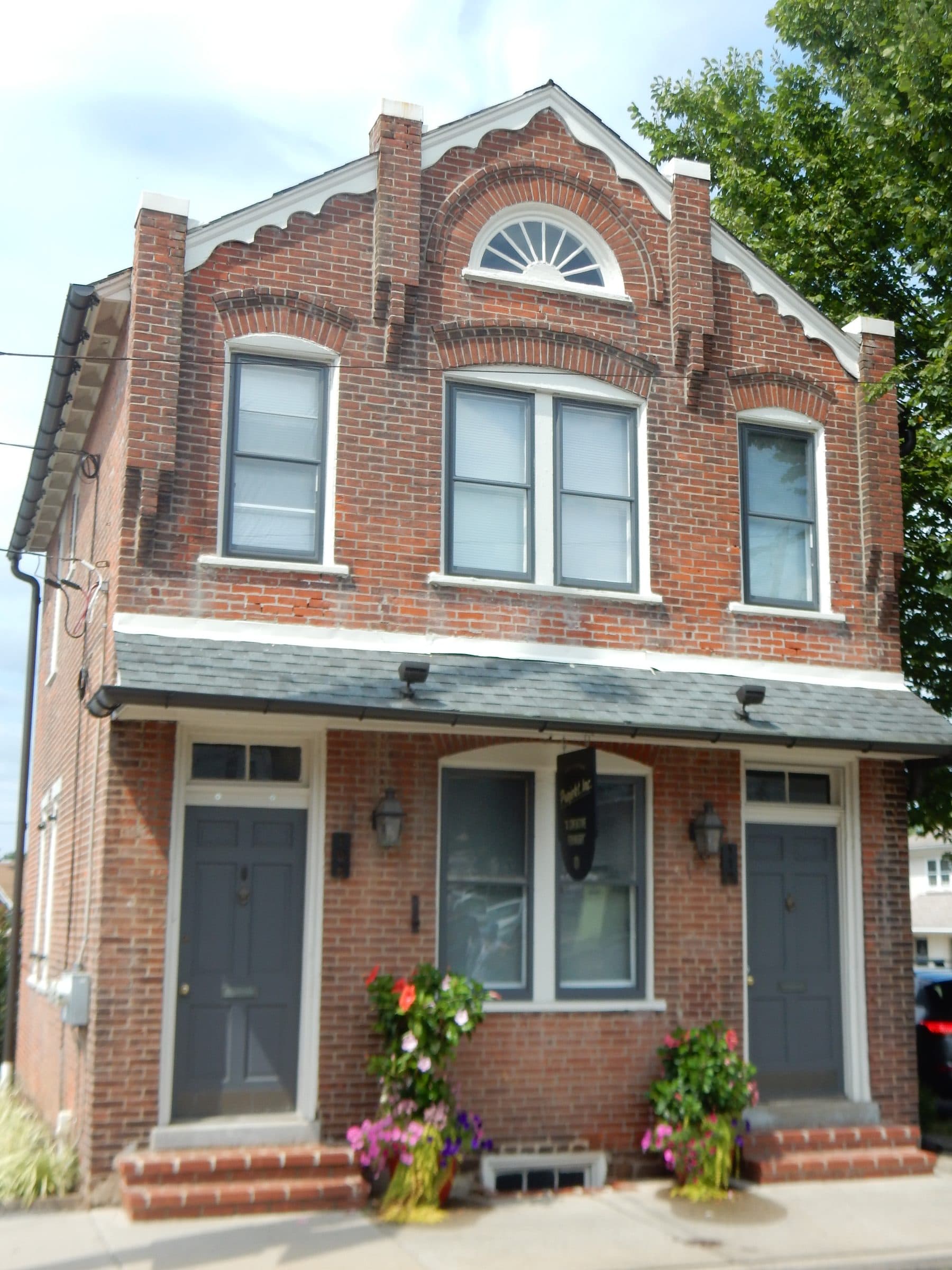 A brick Victorian twin on East Walnut Street in North Wales, Pennsylvania, with arched brickwork over the windows, a fanlight in the gable and flowers on the front steps.