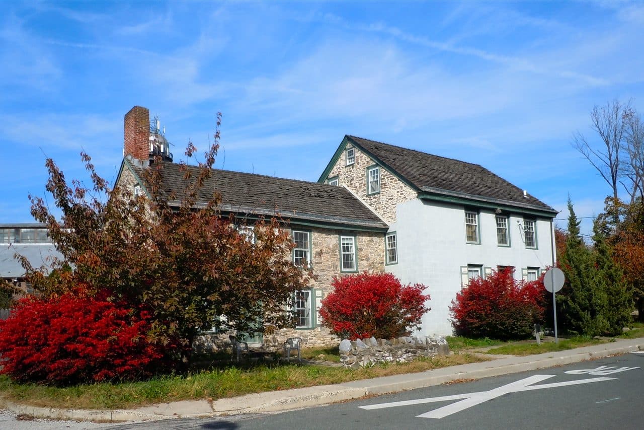The historic Miller’s House in Conshohocken, Pennsylvania, a white and fieldstone house with red autumn shrubs along the street.