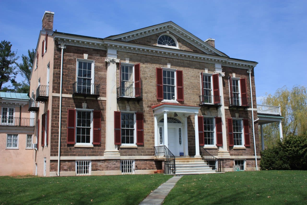 Highlands Mansion in Fort Washington, Pennsylvania, a Georgian stone house with red shutters and a columned entrance above a sloping lawn.