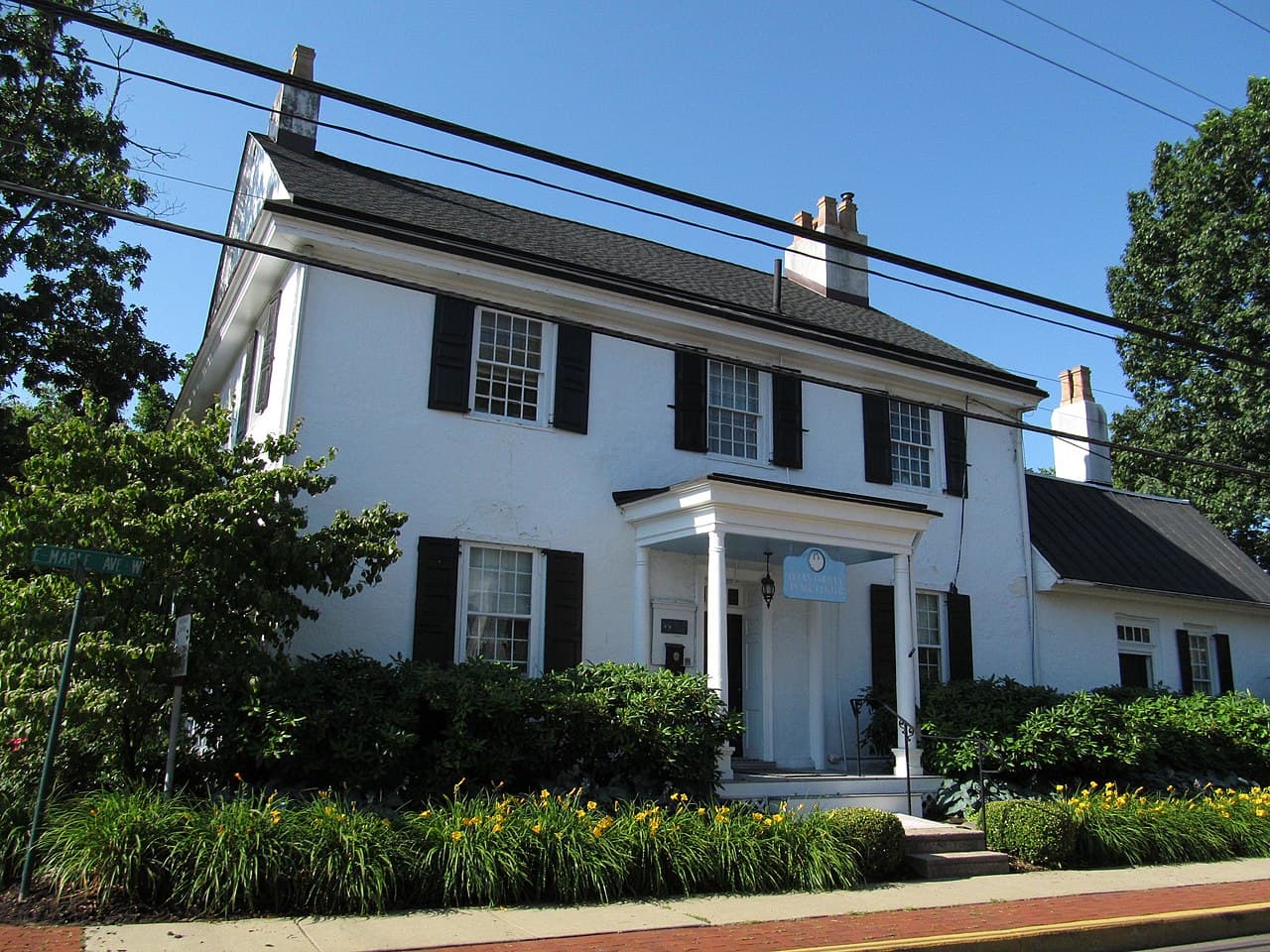 A white stucco colonial-era house with black shutters and a columned entry porch on Maple Avenue in the historic borough of Langhorne, Pennsylvania.
