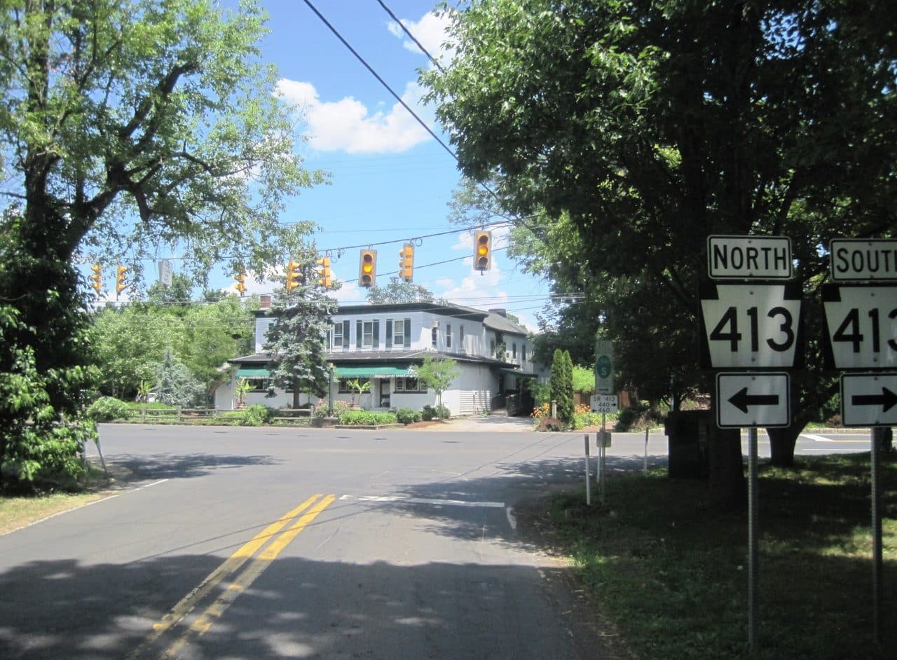 The crossroads at Pineville, Pennsylvania, with Route 413 route markers and the village buildings under trees beyond.