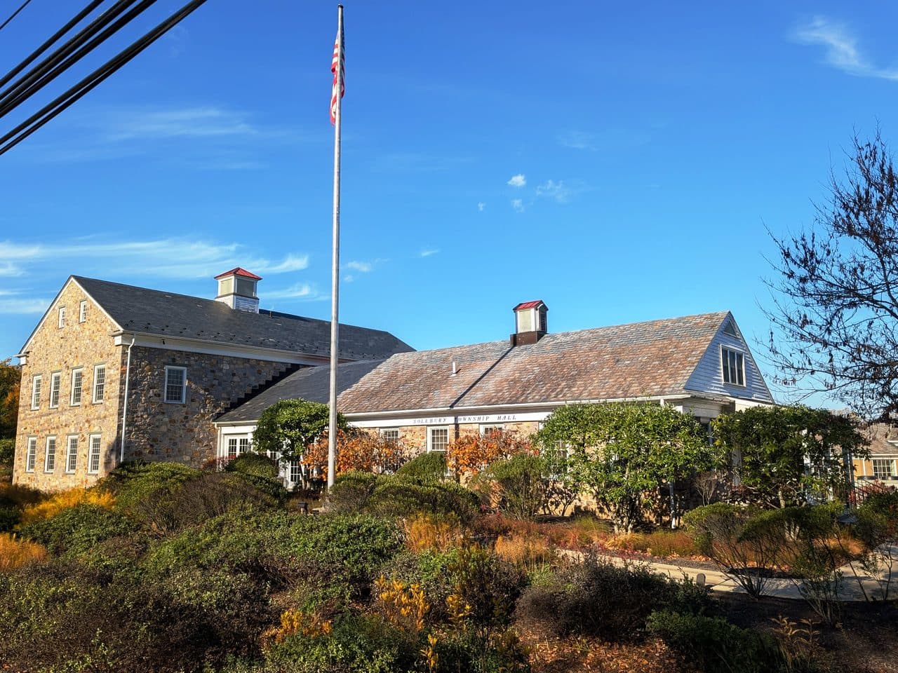 Solebury Township Hall in Bucks County, Pennsylvania, a fieldstone building with dormer windows behind a flagpole and shrub planting.